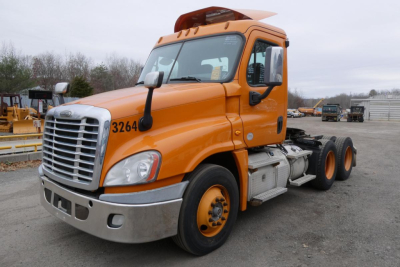 Orange Freightliner Cascadia 125 daycab truck parked in a yard, front-left view showing cab, grille, headlights, bumper, and side steps.