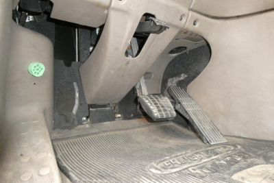 Footwell area of a Freightliner Cascadia 125 cab showing pedals and floor mat.