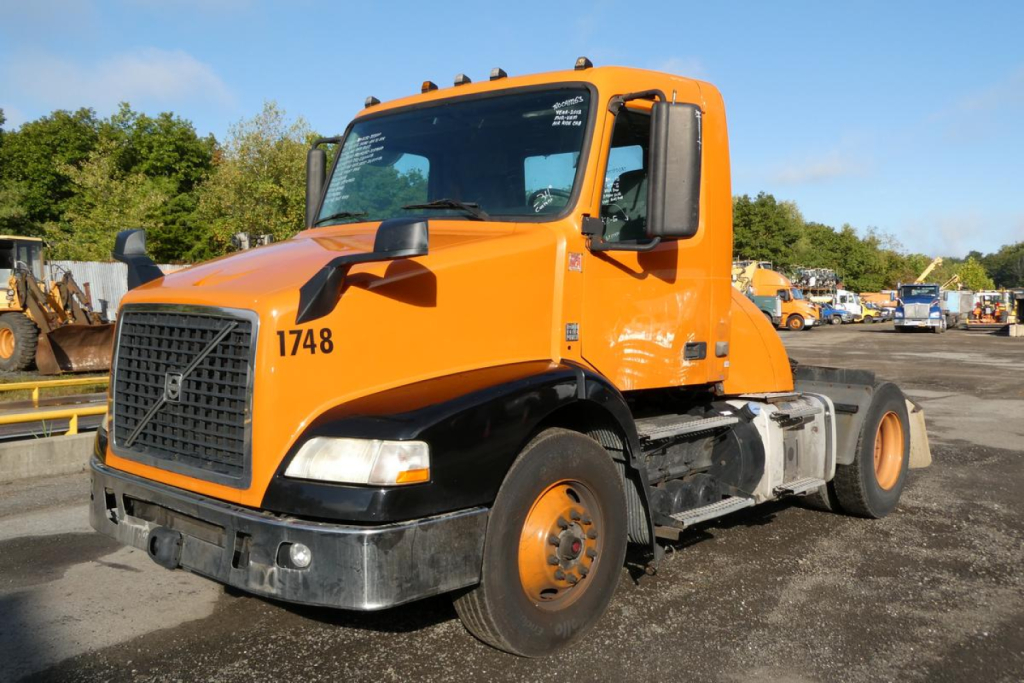 Volvo VNM42T conventional daycab truck in orange, front three-quarter view, showing cab, grille, headlights, and VIN plate area; stock number 0917253 visible.
