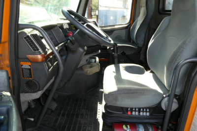  Volvo VNM42T cab interior showing steering wheel, dash, gray driver seat, and pedal area.