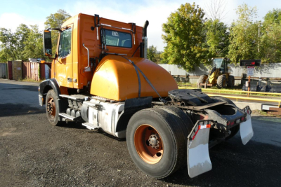 Front-left view of a 2012 Volvo VNM42T conventional daycab dump truck in orange with a large rear vacuum tank, wheels, and rear mud flaps.