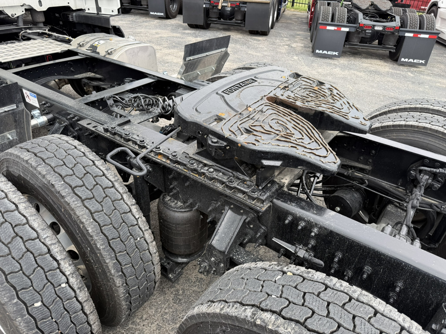 Mack AN64T conventional daycab chassis showing rear dual axles and fifth wheel with tarred deck; black paint and road grime