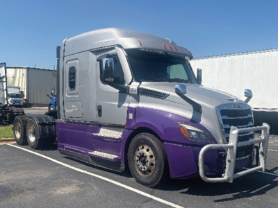 Truck front-left side of a Freightliner Cascadia126 cab in silver and purple with a large bull bar, showing side mirrors and aerodynamic features.