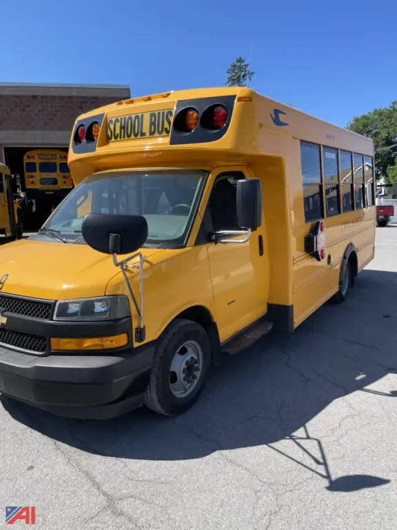 School bus side and front view showing bright yellow GM Express G3500 with 'SCHOOL BUS' sign on top, black front bumper, mirrors, and passenger windows.
