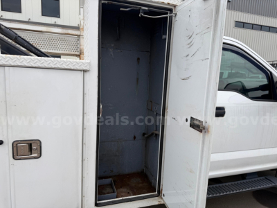 Truck cargo area/utility box in open rear compartment of a white Ford F-550 service vehicle showing empty metal interior and door hinges.