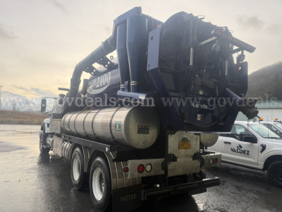 Waste vacuum truck rear view showing large vacuum system and water tank on chassis with hoses and engine housing visible.