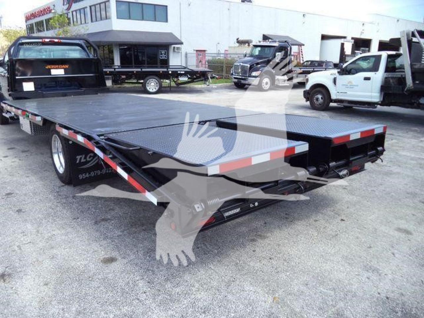 Flatbed tow truck trailer with black diamond plate surface and red/white reflective tape, Silverado 6500HD truck bed in background.