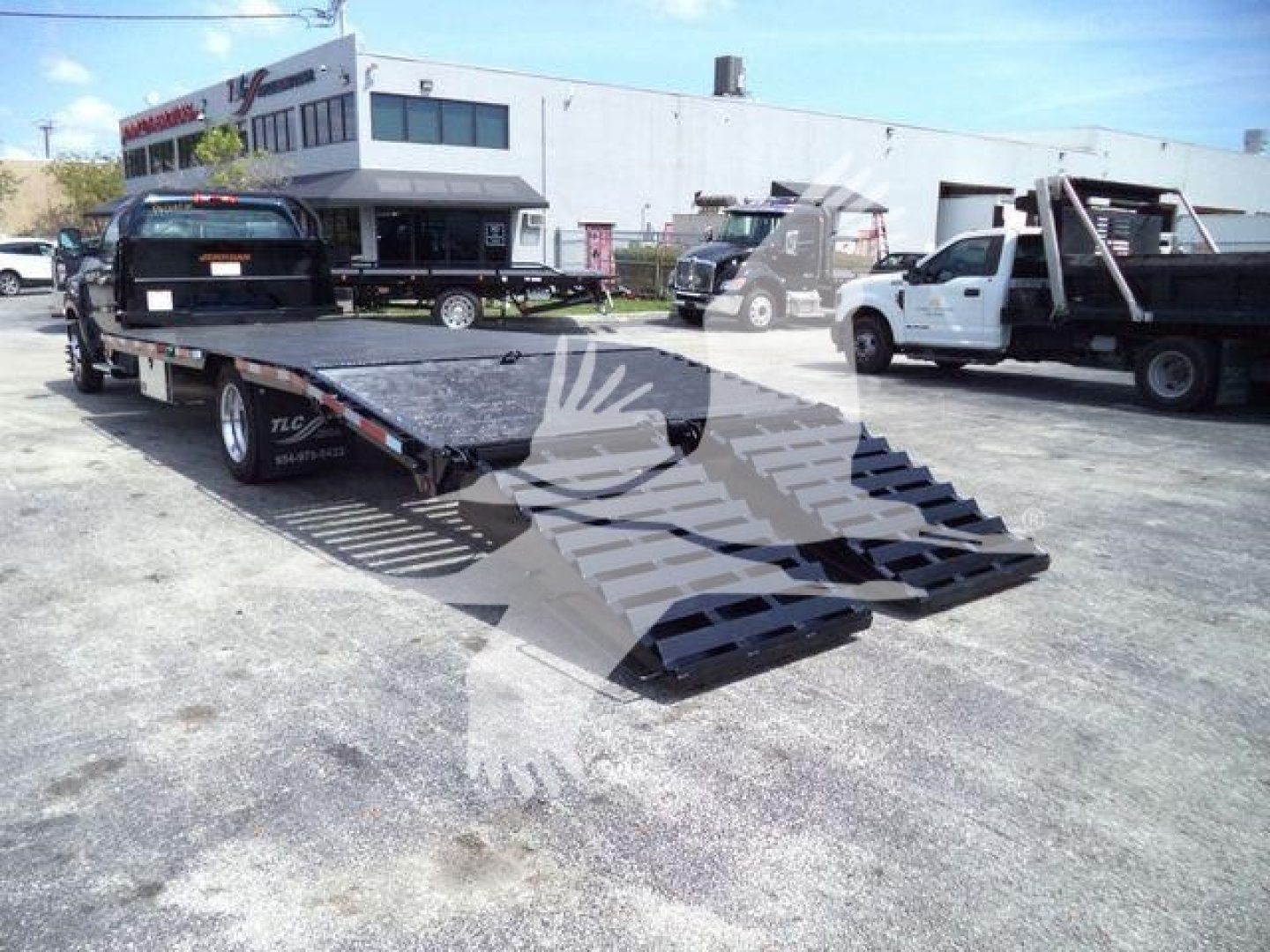 Chevrolet Silverado 6500HD flatbed truck with wheeled ramps and a car on the bed in a used vehicle lot.