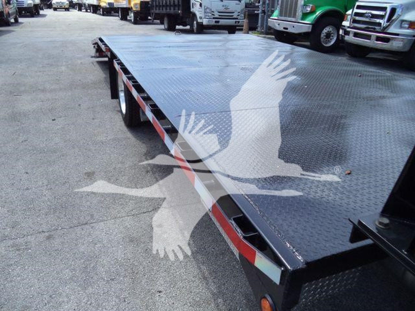 Flatbed truck bed on a new Chevrolet Silverado 6500HD with diamond plate surface and reflective edge marker, surrounding lot of trucks.