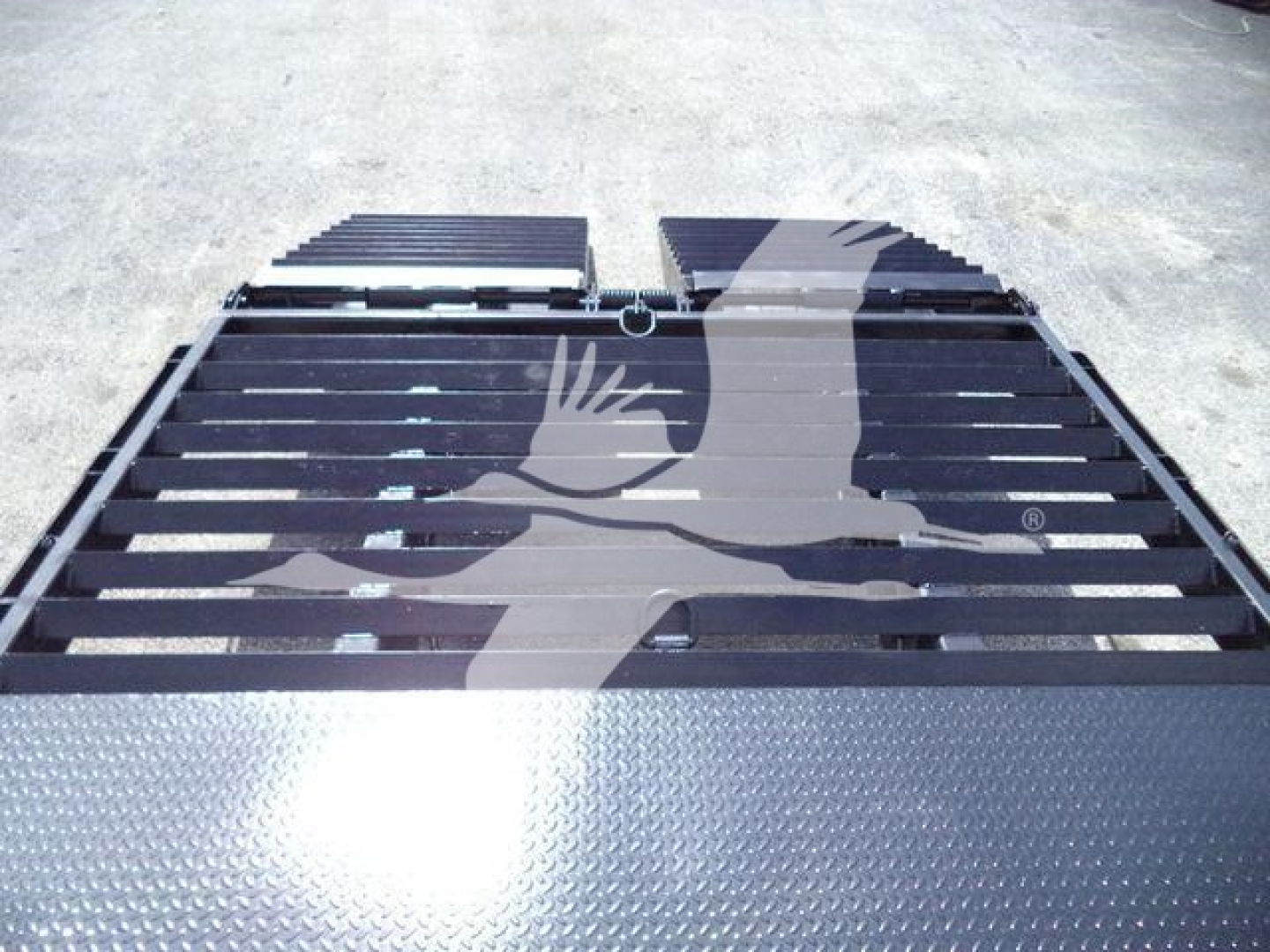 Truck bed with ramp-style pieces and metal diamond plate along edge. The image shows a black flatbed surface with slats and a graphic watermark across.