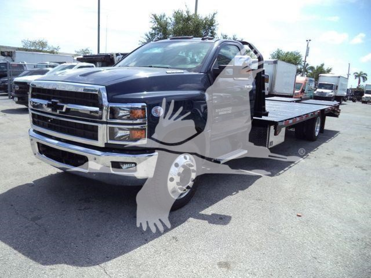 Chevrolet Silverado 6500HD tow truck in a showroom lot with flatbed; front grille and chrome bumper visible.