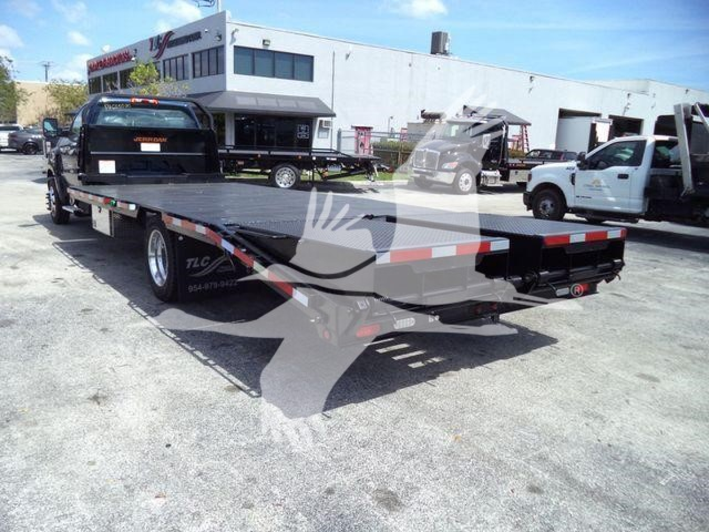 Chevrolet Silverado 6500HD flatbed truck with ramp, rear view showing flatbed and dual rear wheels, in a dealership lot.