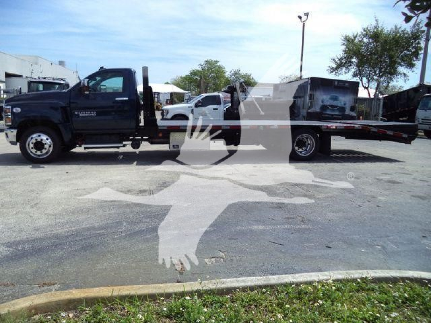 Chevrolet Silverado 6500HD flatbed tow truck side view with black cab and extended flatbed.