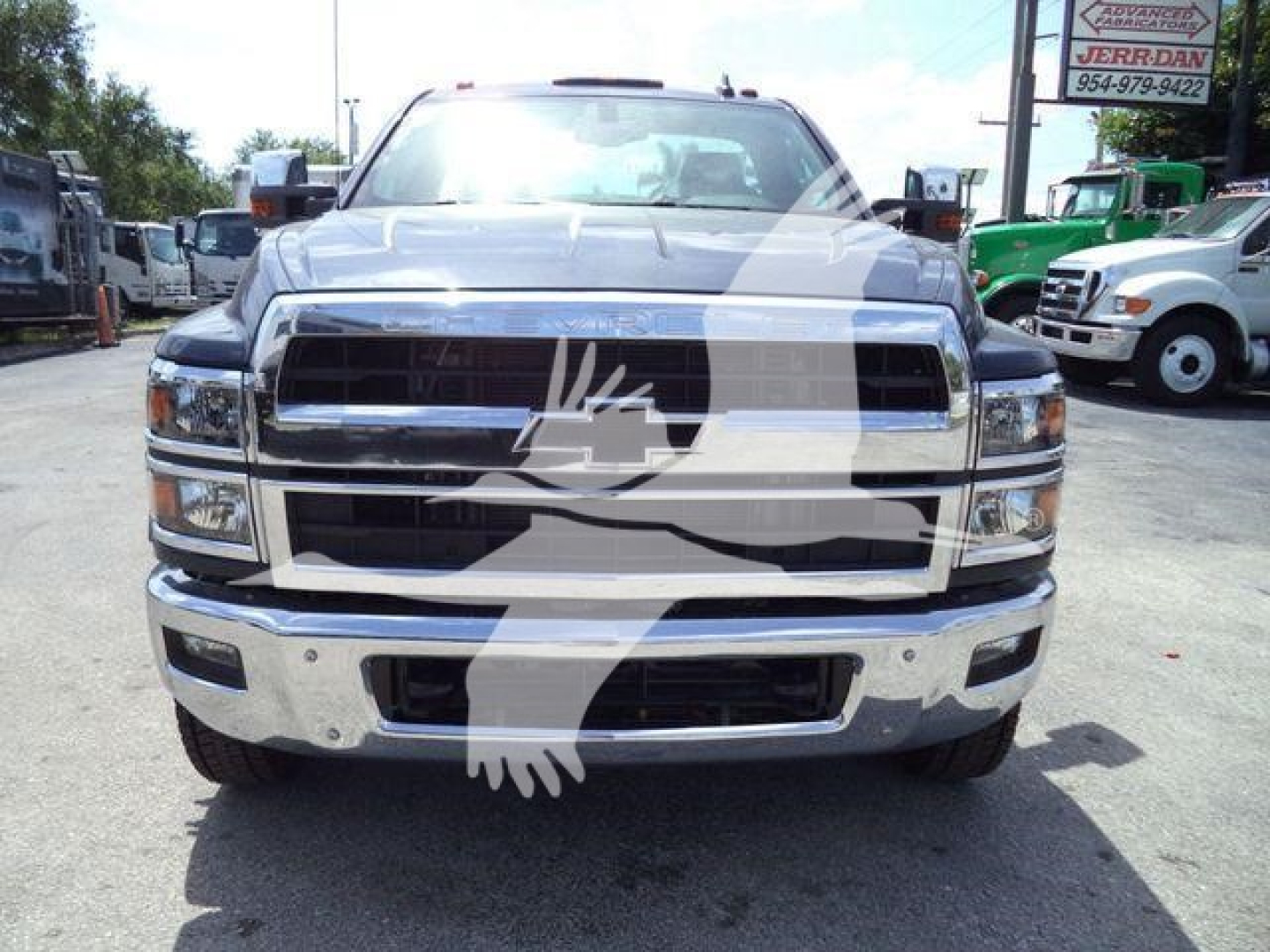 Chevrolet Silverado 6500HD front view showing chrome grille, bumper, and headlights with dealership lot in background.