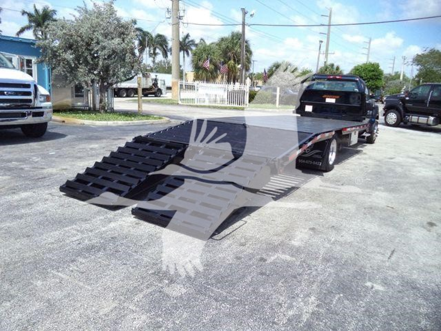 Truck bed with ramp trailer attached to a Chevrolet Silverado 6500HD on a dealership lot, front left view, ramps folded down for loading, other vehicles in background.