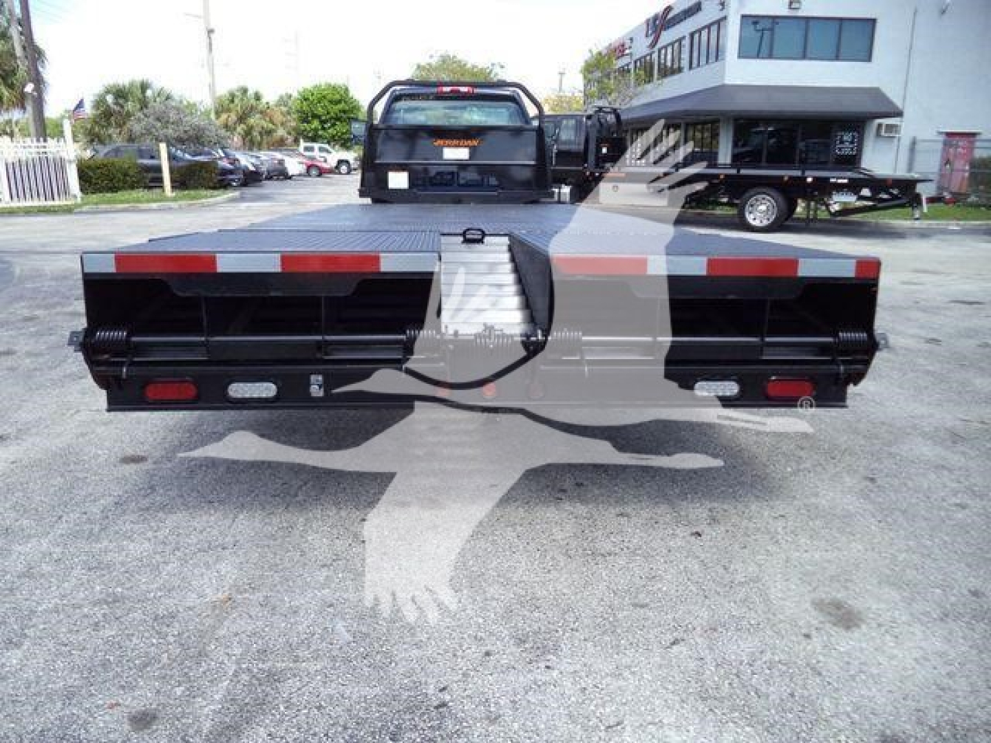 Rear view of a 2023 Chevrolet Silverado 6500HD flatbed with ramp. Visible bumper lights and reflective striping along the back edge.