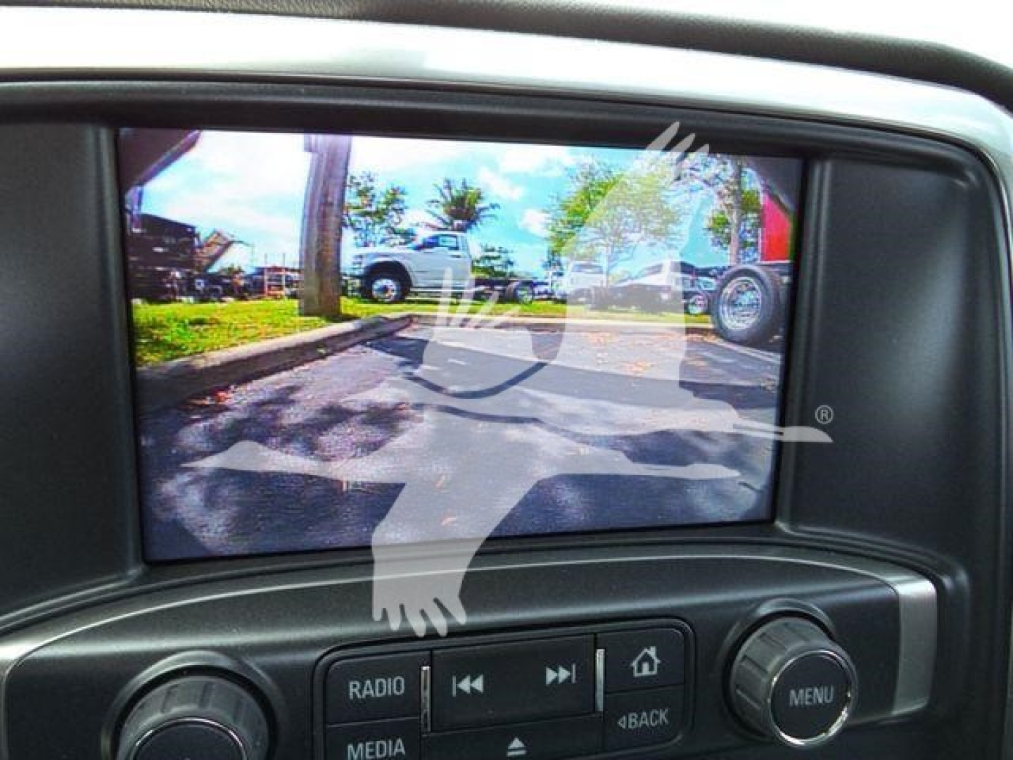 Truck interior showing a dashboard screen with a reversed watermark. Inset image displays a rearview monitor with a parking lot and vehicles visible.
