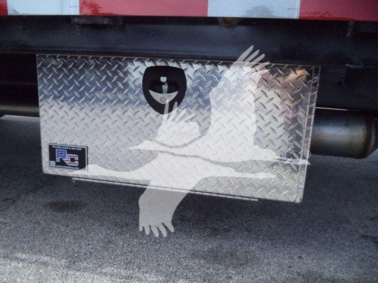 Rear underbody toolbox with diamond plate and Rigid Tool Discovery logo. A small blue/black sticker near left side reads R3 or R? with metal panel.