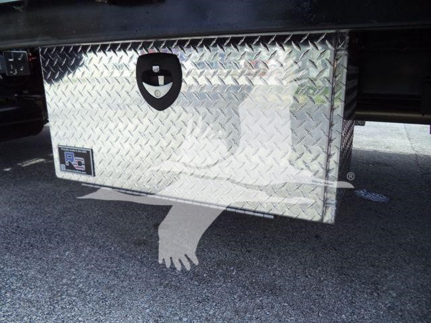 Aluminum diamond plate tool box mounted under a Chevrolet Silverado 6500HD truck chassis showing latch and handle.