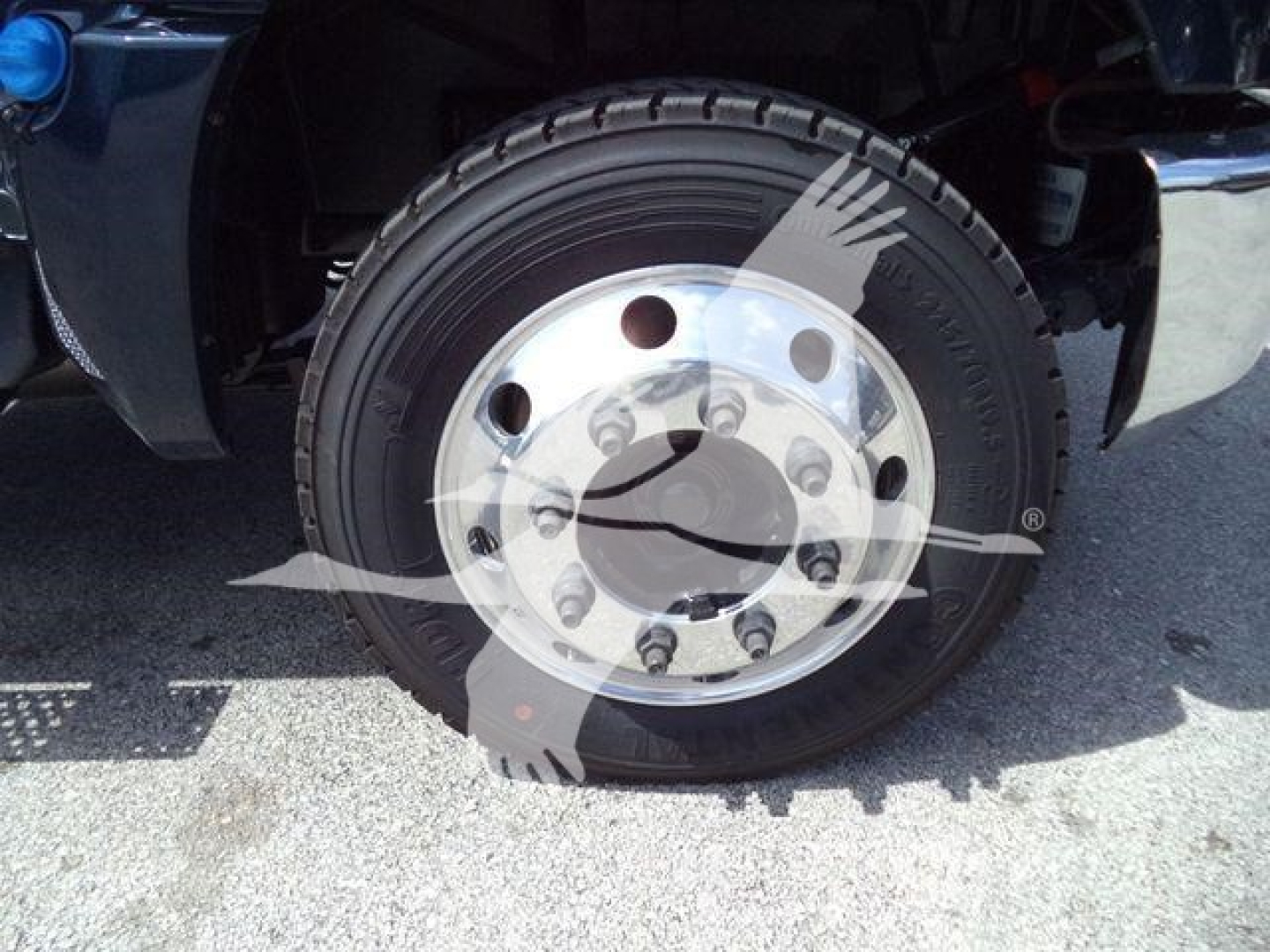 Front wheel of a Chevrolet Silverado 6500HD with chrome hub and radial tire, visible wheel lug nuts and fender.