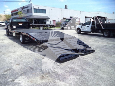 Chevrolet Silverado 6500HD flatbed truck with wheeled ramps and a car on the bed in a used vehicle lot.