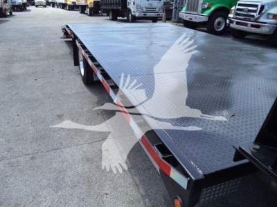 Flatbed truck bed on a new Chevrolet Silverado 6500HD with diamond plate surface and reflective edge marker, surrounding lot of trucks.