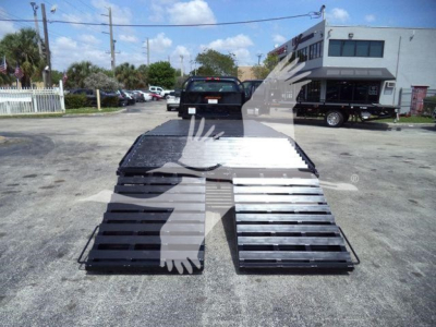 Chevrolet Silverado 6500HD flatbed ramp trailer in a dealership lot, with a large curbside ramp and asphalt surface.