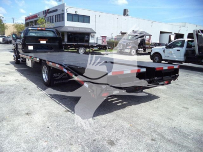 Chevrolet Silverado 6500HD flatbed truck with ramp, rear view showing flatbed and dual rear wheels, in a dealership lot.