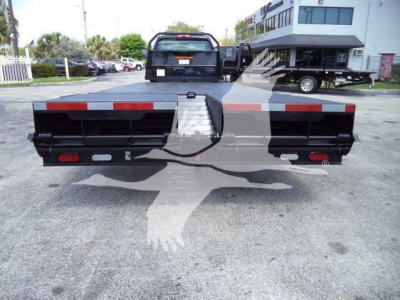 Rear view of a 2023 Chevrolet Silverado 6500HD flatbed with ramp. Visible bumper lights and reflective striping along the back edge.