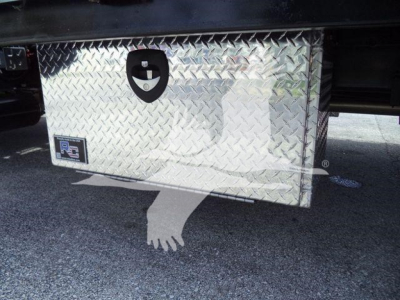 Aluminum diamond plate tool box mounted under a Chevrolet Silverado 6500HD truck chassis showing latch and handle.