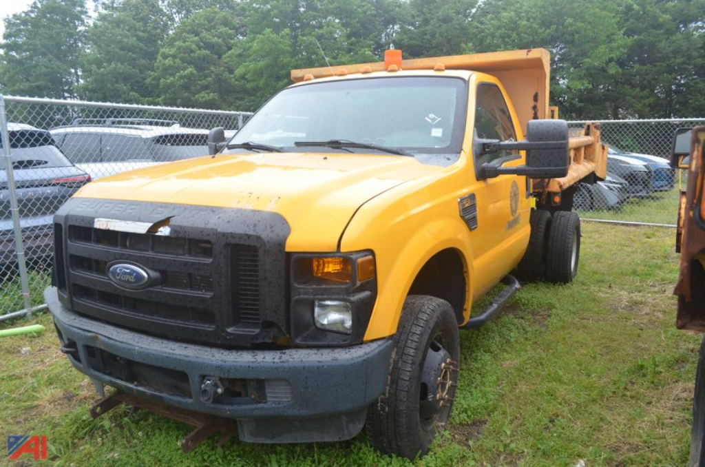 2009 Ford F-350 Super Duty dump truck in yellow with dump bed raised, front grille and bumper, large side mirrors, on a grassy lot.