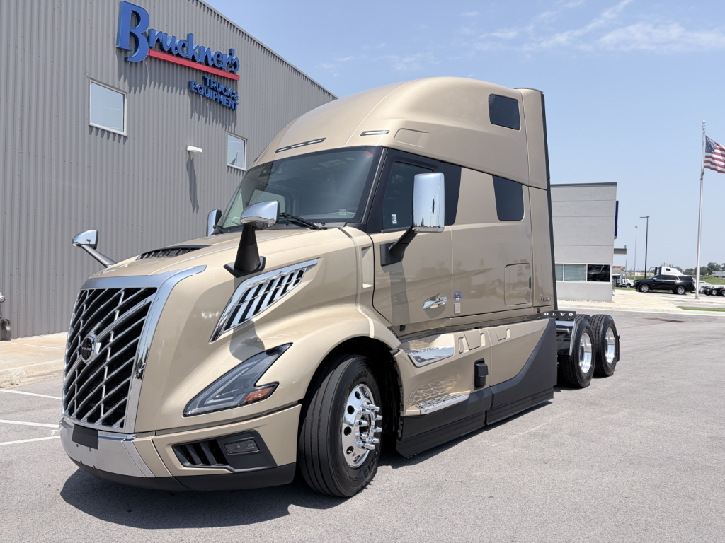 Volvo VNL 64T860 tractor-trailer cab in beige showing front grille, headlights, and side mirrors, with sleeper windshield and logo details.