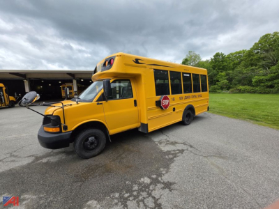 Bus side view showing 2014 Chevrolet Express G4500 mini school bus in yellow with stop sign and school markings