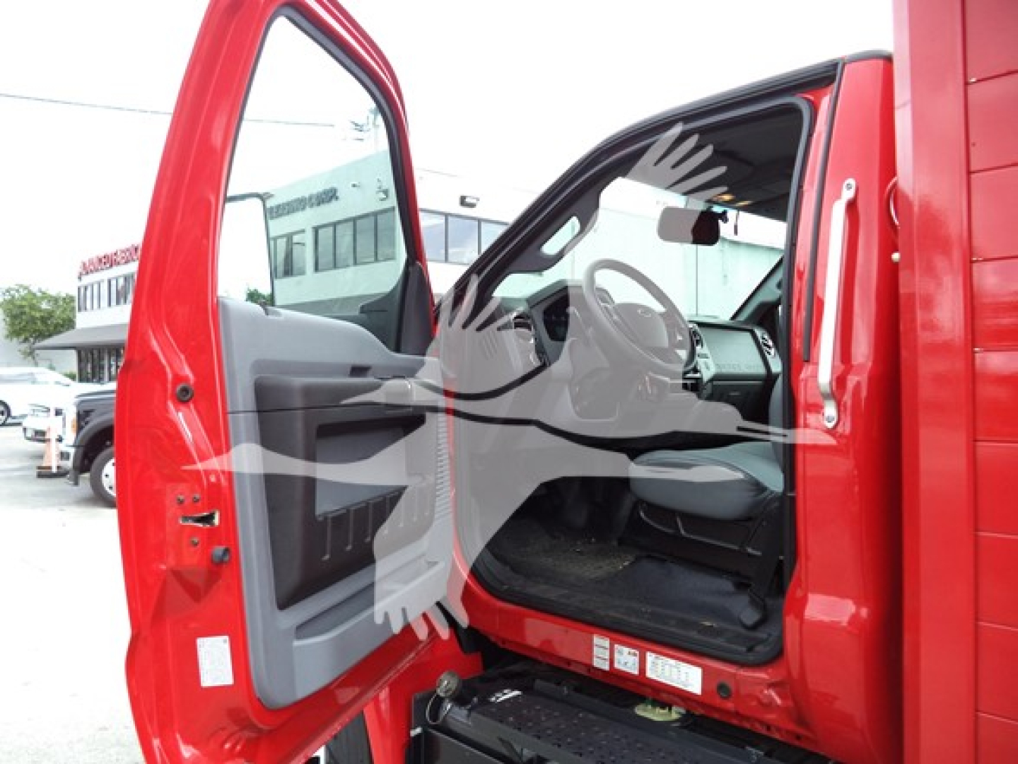 Ford F650 cab interior view with open driver door showing steering wheel, dashboard, and gray cloth seat.