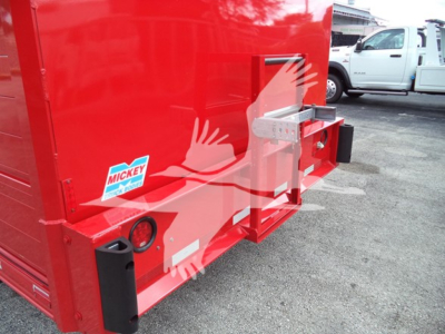 Rear view of red Ford F650 dump body showing tailgate latch and warning label, side sticker, and welded hitch plate.