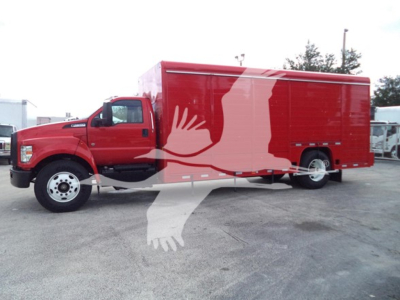 Ford F-Series truck with red box body and white emblem on side, side view showing extended cab and cargo box in a lot.