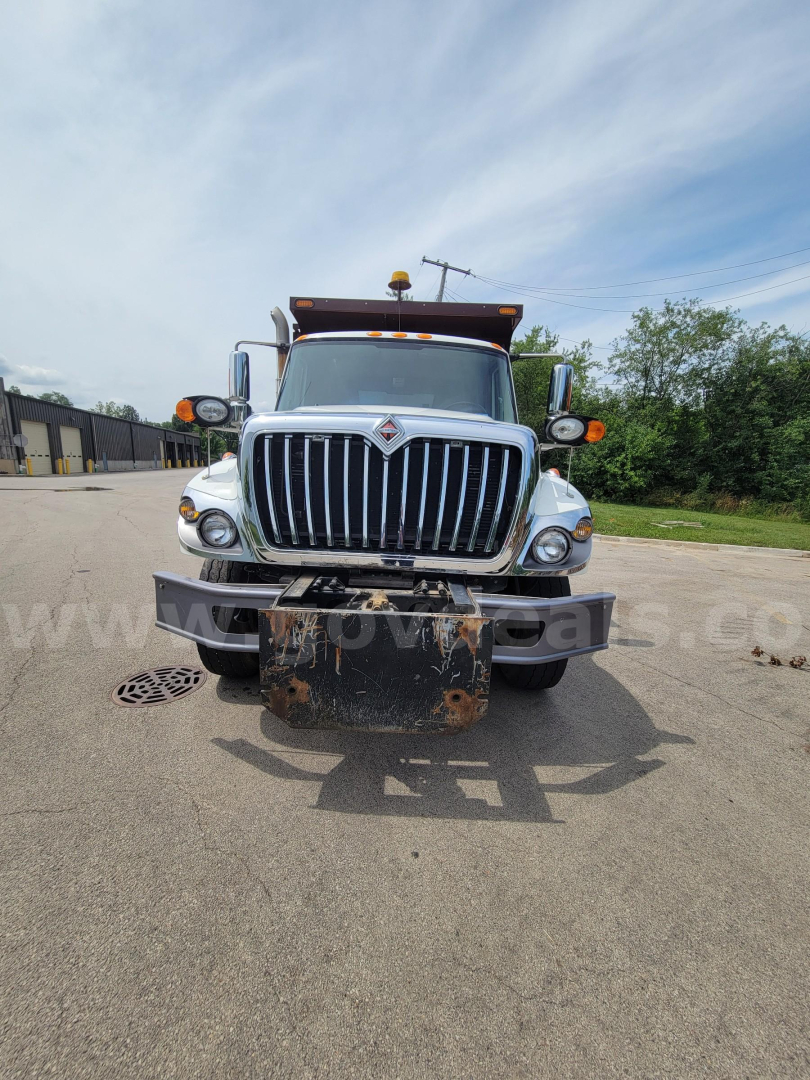 Front view of a dump truck showing the grille and bumper with a rusted plow hitch plate and amber clearance lights; International emblem on the grille.