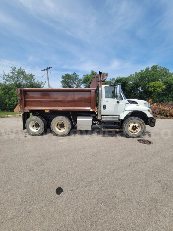 Dump truck side view showing white cab and brown dump bed, International 7400 series, 6x4 axle configuration, three rear axles, daytime outdoor lot