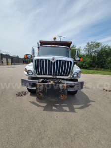 Front view of a dump truck showing the grille and bumper with a rusted plow hitch plate and amber clearance lights; International emblem on the grille.