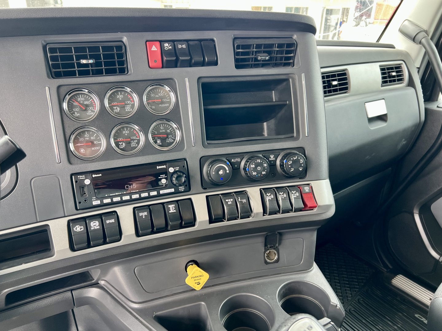 Dashboard of a Kenworth truck cockpit with multiple gauges, vents, and a yellow key tag hanging from the ignition area; visible labels include circular gauges and various switches.