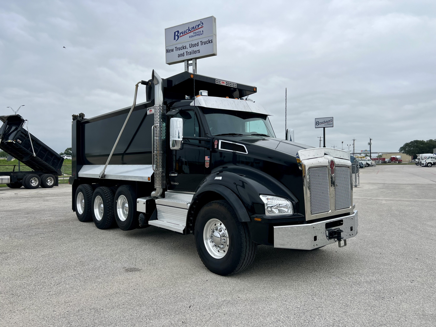 Kenworth T880 dump truck in a parking lot, black cab, 6x4 drive, aluminum dump body, chrome front bumper, side steps, dual rear axles.