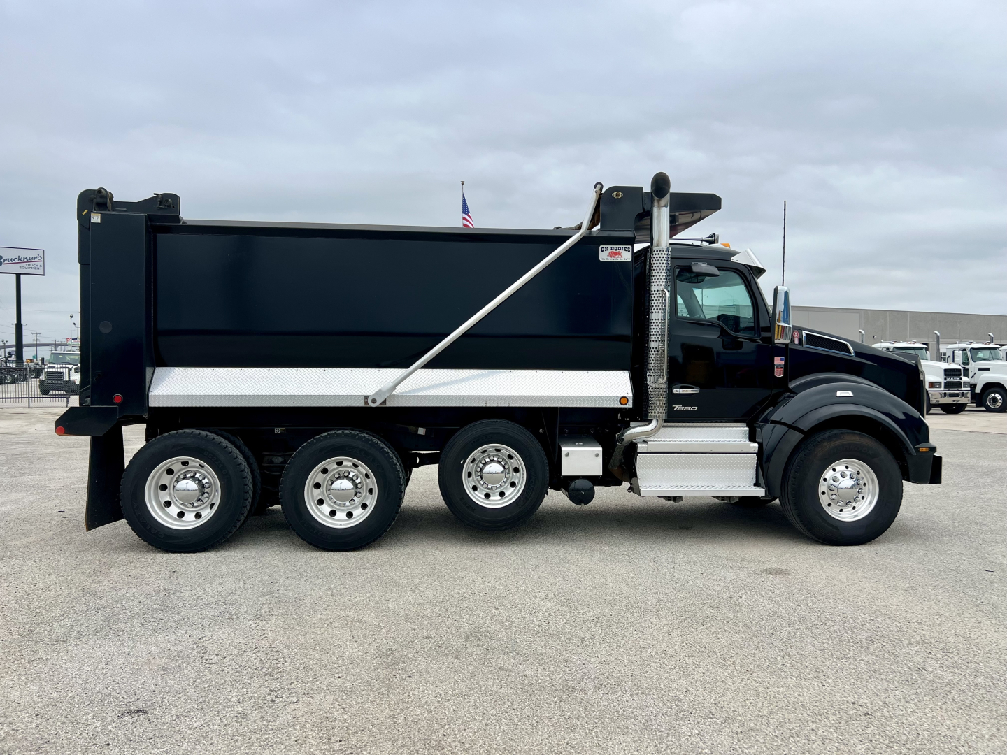 Kenworth T880 dump truck side view showing black dumped body, chrome wheels, and side cab features with Vin 1NKZX4TX2TJ209434 plate not visible.
