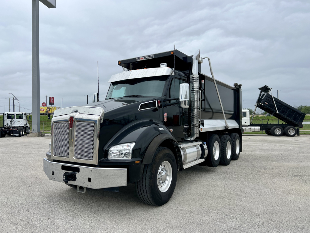 Kenworth T880 dump truck in service view showing dump body raised on right side with chrome front bumper and dual rear axles.