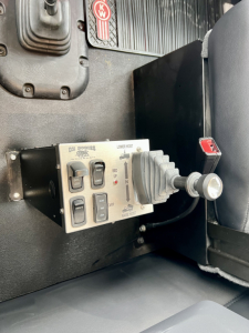 Kenworth T880 dump interior showing control lever and joystick with labeled switches and two toggles in a panel.