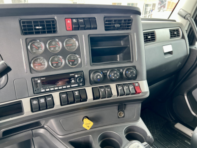 Dashboard of a Kenworth truck cockpit with multiple gauges, vents, and a yellow key tag hanging from the ignition area; visible labels include circular gauges and various switches.