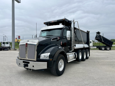 Kenworth T880 dump truck in service view showing dump body raised on right side with chrome front bumper and dual rear axles.