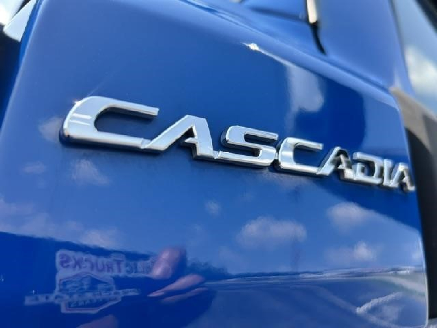 Close-up of blue Freightliner Cascadia 126 front badge reading 'CASCADIA' on the hood.