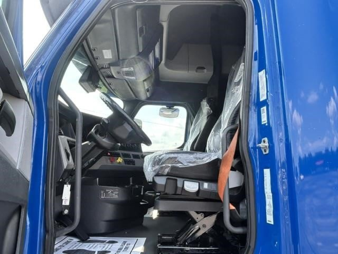 Freightliner Cascadia 126 cab interior view from driver door showing steering wheel, dashboard, and driver's seat with plastic covering.