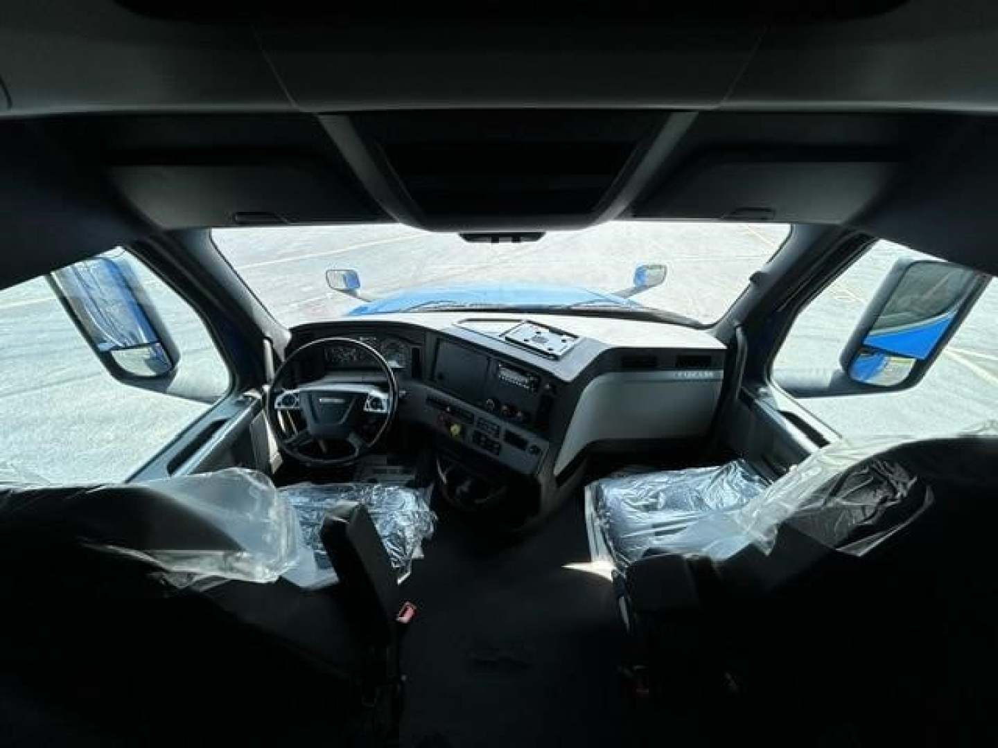 Cab interior of a 2022 Freightliner Cascadia 126 sleeper showing steering wheel, dashboard, and plastic-covered seats.