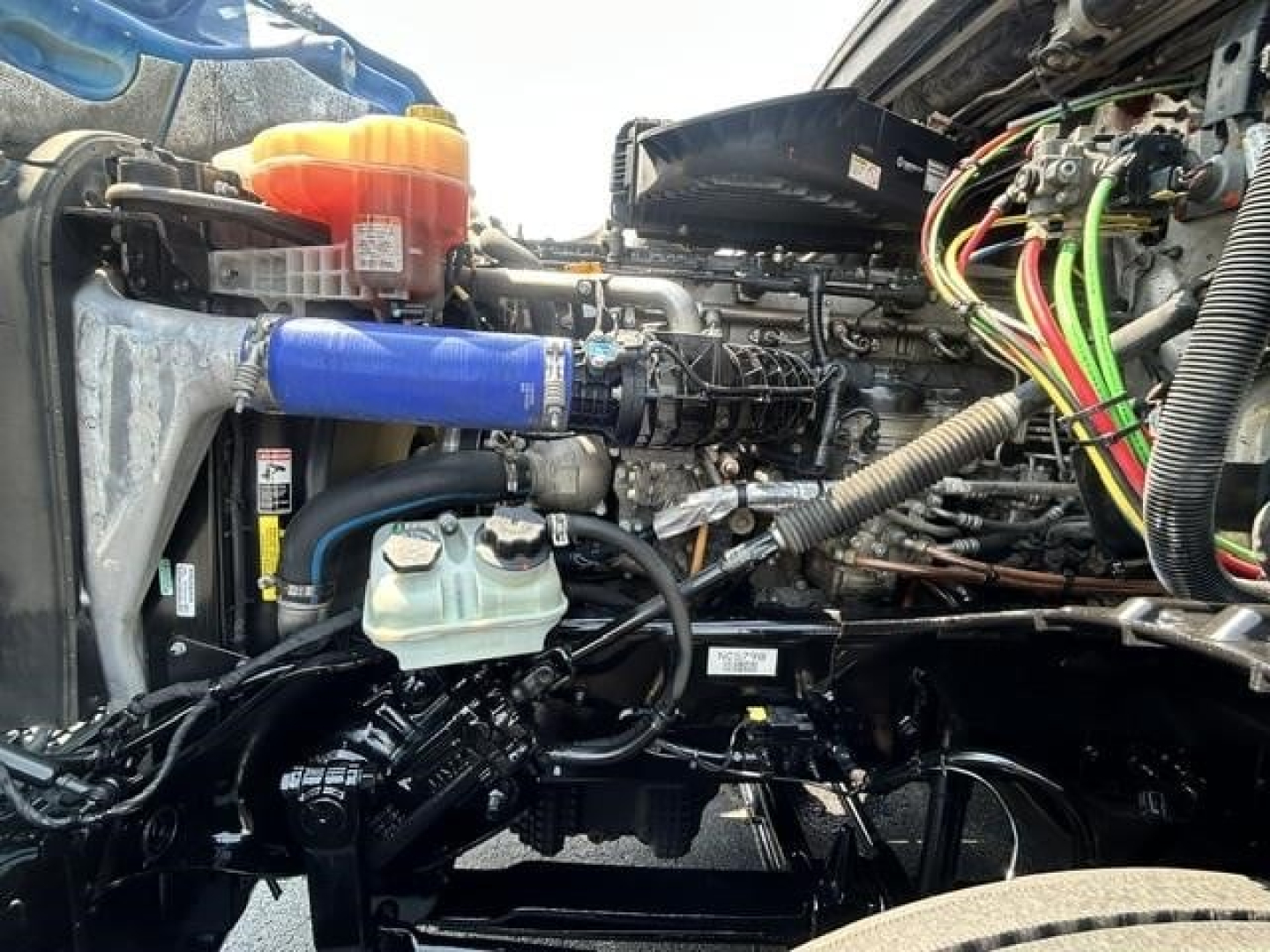 Engine bay of a 2022 Freightliner Cascadia 126 conventional sleeper showing coolant reservoir, blue discus hose, wiring harness, and various engine components.